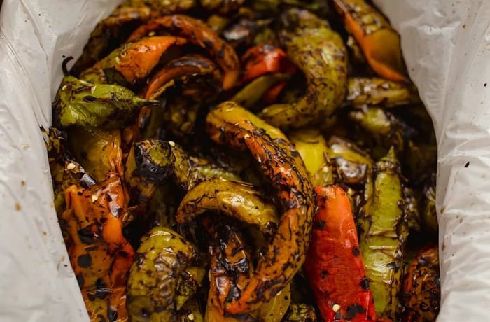 Red and green chiles with charred skin are stacked in a plastic bag.