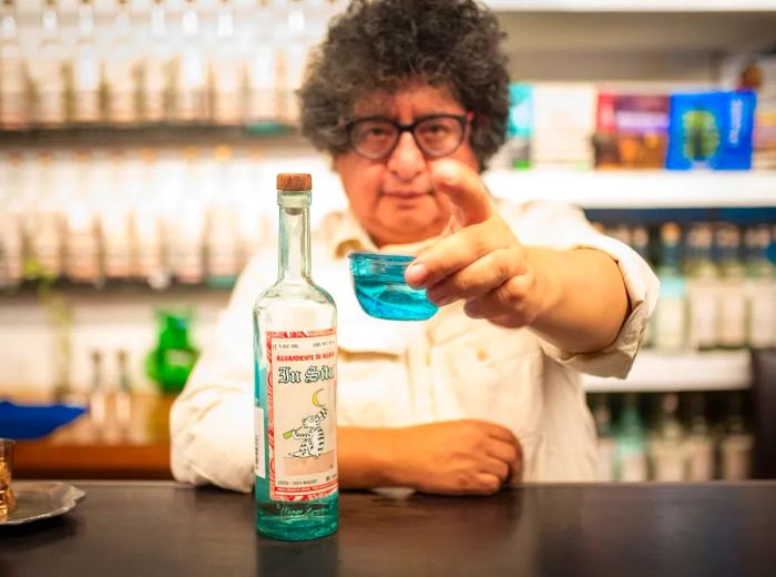 A man passes a cup of mezcal over the bar.