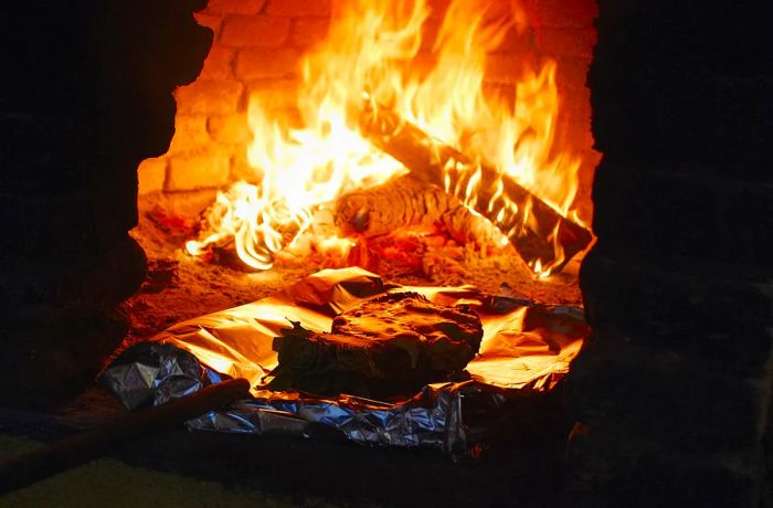 A roaring wood fire blazes inside the opening of an oven, as a pineapple is placed inside.