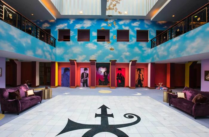 Prince's symbol is prominently displayed on a white floor, with images of the artist throughout various stages of his career showcased in cubbyholes on a sky-blue wall adorned with clouds, complemented by two balconies flanking the atrium.