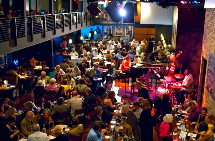 Interior of the Dakota Jazz Club and Restaurant, bustling with patrons seated at tables while a live band performs on an elevated stage.