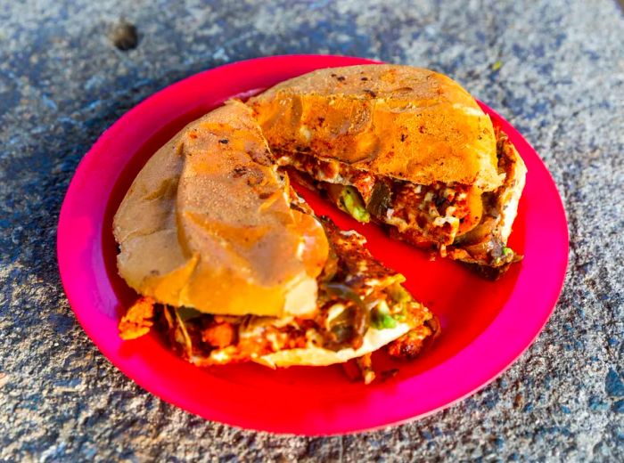 A stuffed torta, halved and resting on a red plastic plate on a concrete surface.