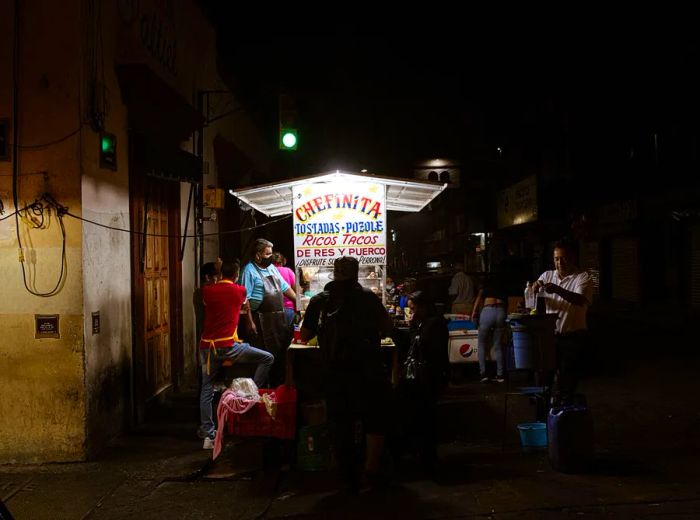 A brightly lit street cart attracts a crowd at night.