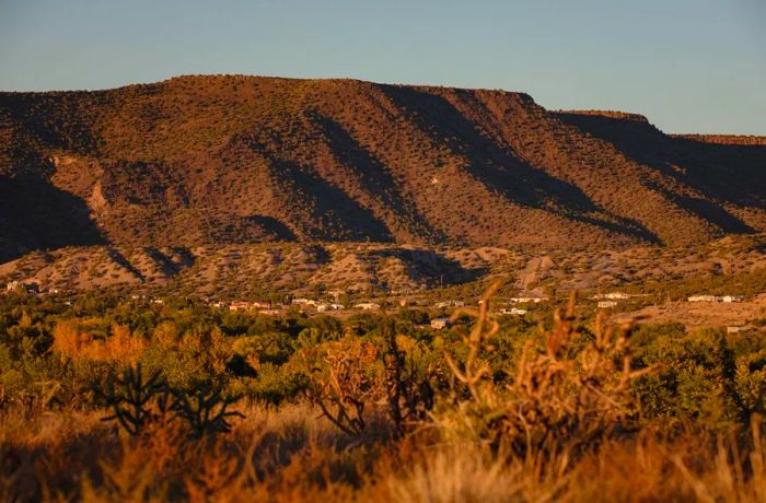 A few modest homes are scattered across a desert landscape, with a tall mesa rising in the background.