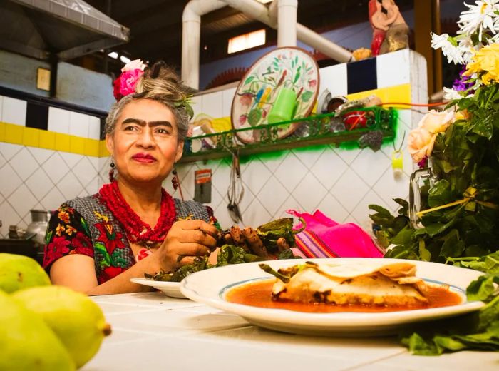 A woman dressed as Frida Kahlo sits at a table adorned with delicious food.