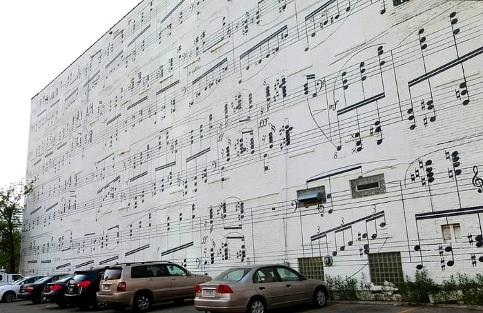 A vibrant mural on the side of the Schmitt Music Building, depicting a large sheet of music with black notes set against a white backdrop.