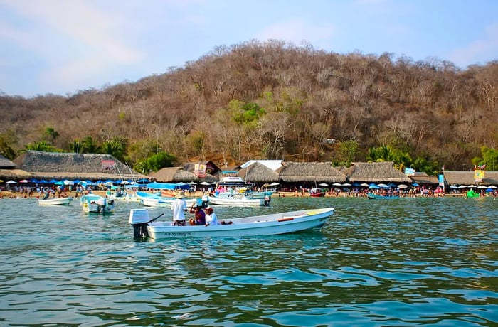 A boat gently sways in the foreground, with the palapa-covered beach in the background.