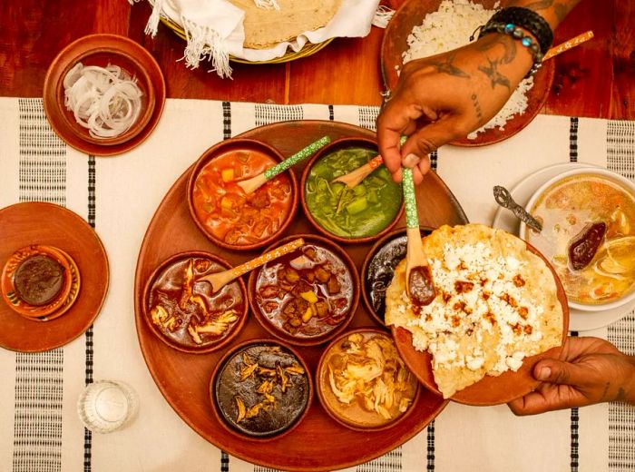 An aerial view shows a woman’s hands carefully ladling small sauces onto a piece of masa.