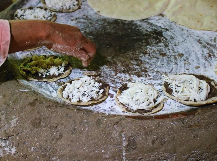 An arm reaches over a comal, skillfully preparing masa discs.