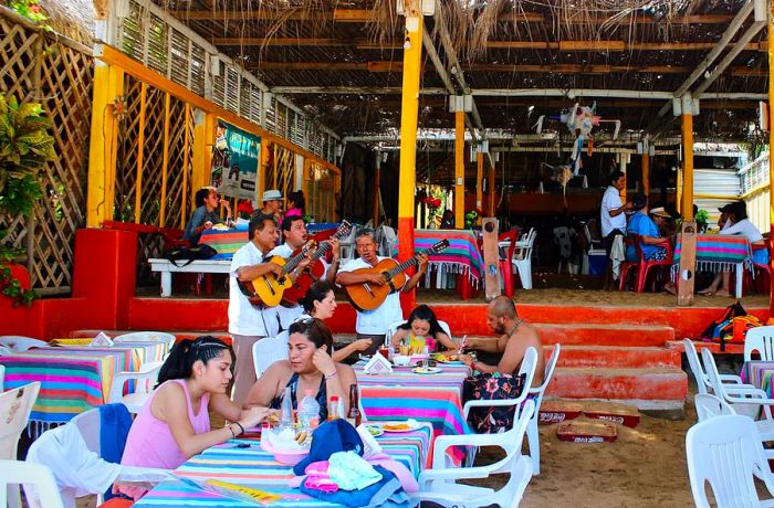 Guests dine at sandy tables while live guitarists serenade them.