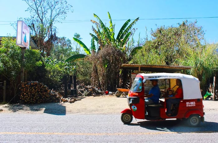 A small three-wheeled vehicle transports passengers through a quaint rural town.