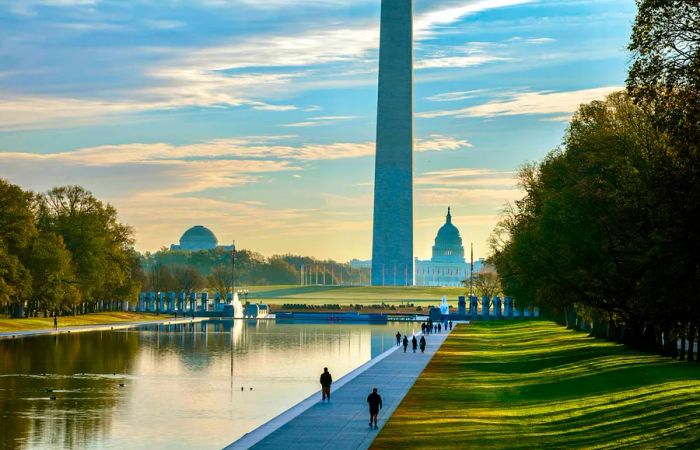 A stunning sunrise illuminates a rectangular pool at the base of a grand monument.