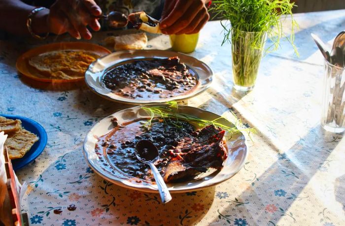 Two bowls of black beans with dried beef rest on a floral tablecloth, illuminated by morning light.