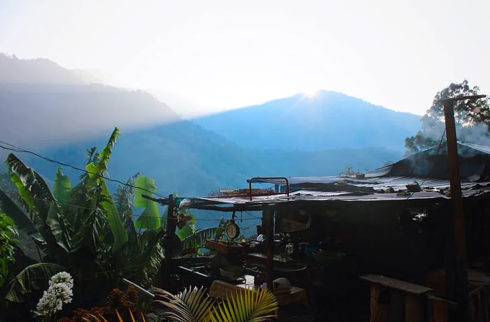 A sunlit mountain cabin rests amidst the scenery.