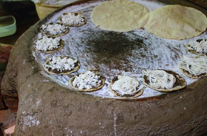 Round memelas sizzle atop a clay comal, adorned with white cheese.