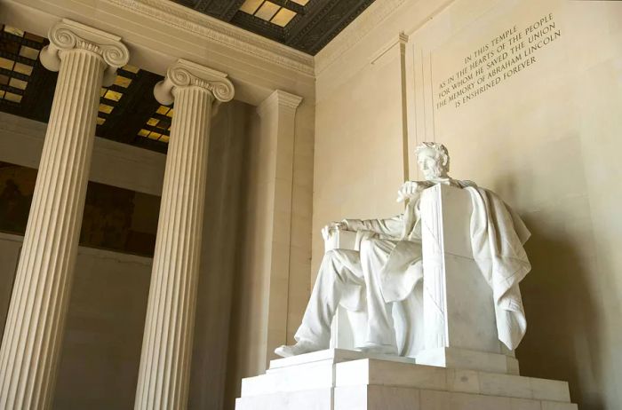 A large white-stone statue of a seated man graces a hall adorned with decorative columns. Above, an inscription reads, 'In this temple as in the hearts of the people for whom he saved the Union, the memory of Abraham Lincoln is enshrined forever.'