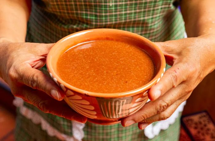 Hands cradle a decorative bowl filled with rich, thick champurrado.