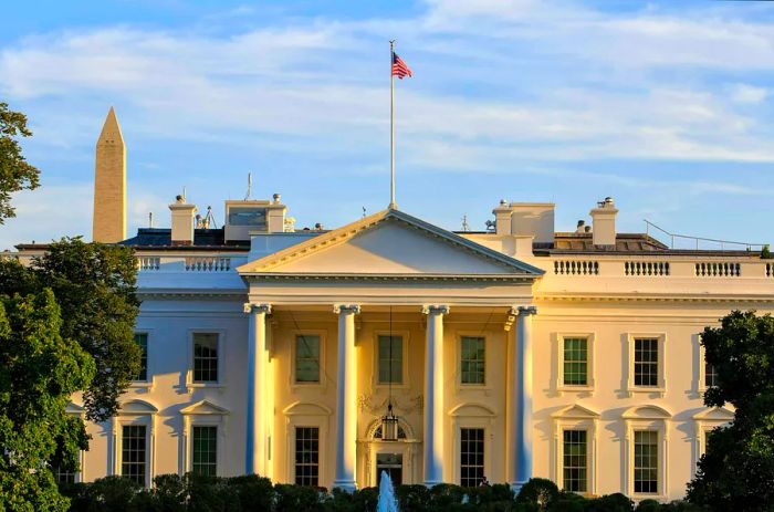 A striking view of the White House, featuring its symmetrical columns and an American flag proudly flying above.