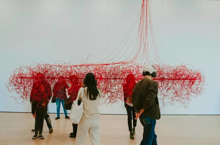 A couple observes a red thread sculpture in a bright white room at SFMOMA.