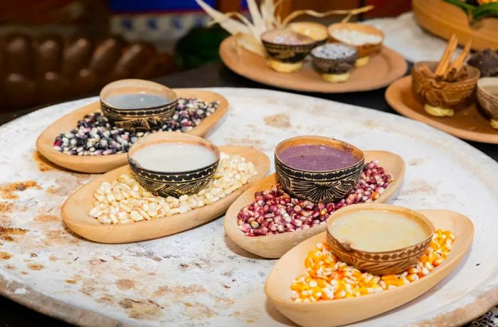 Four small cups filled with liquids of various colors rest atop different mounds of corn kernels.