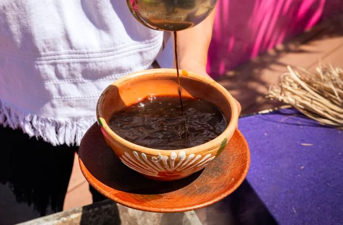 A rich brown liquid is poured into a rustic, colorful ceramic bowl.