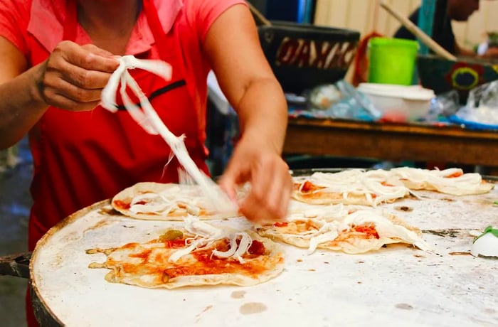 A woman skillfully pulls strings of quesillo to garnish memelas.