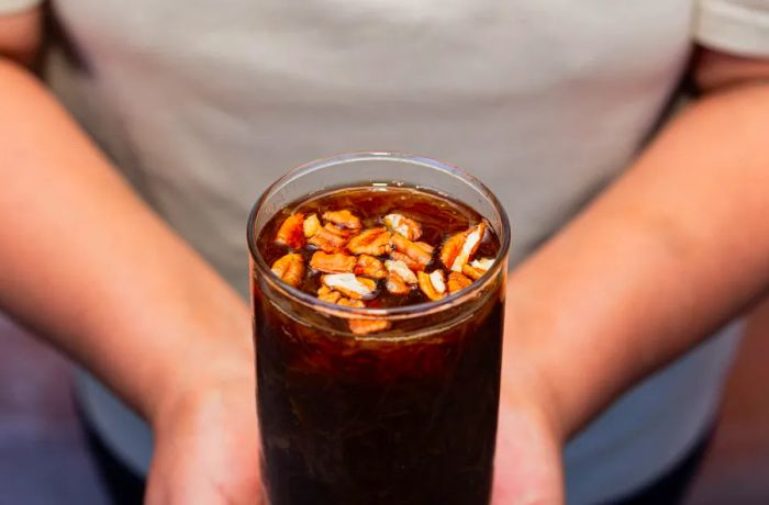 A tall glass features a dark brown liquid topped with nuts.