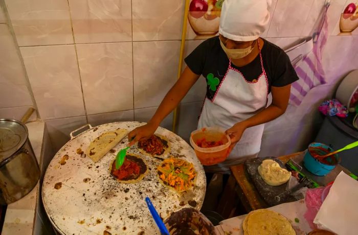 A woman crafts memelas on a cooking surface