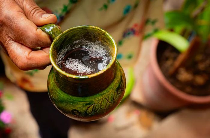 A weathered hand cradles a green ceramic mug.