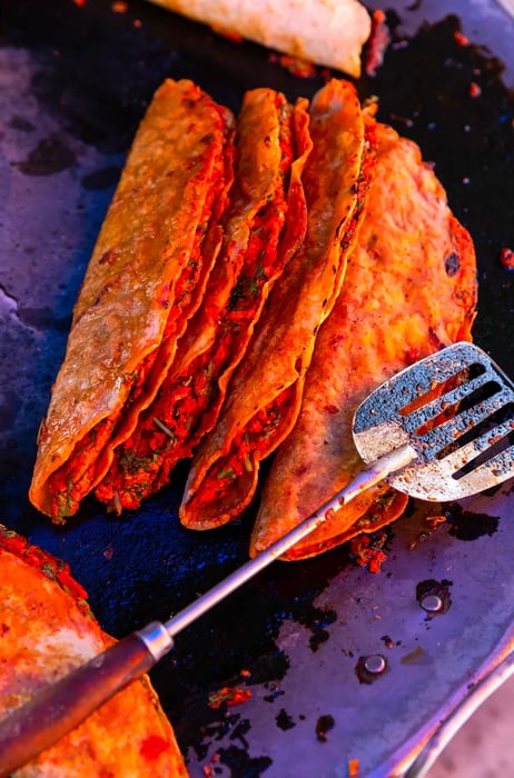 Four empanadas resting on a comal, ready to be served, with a metal spatula nearby.