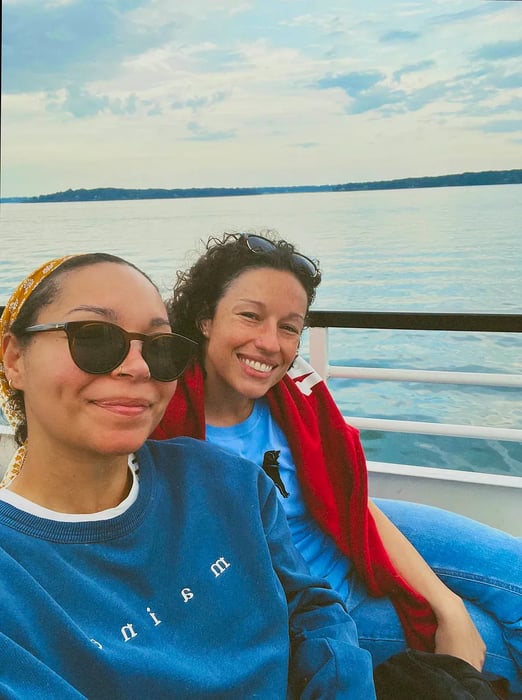 Two women huddle together on the top deck of a boat, smiling for a photo.