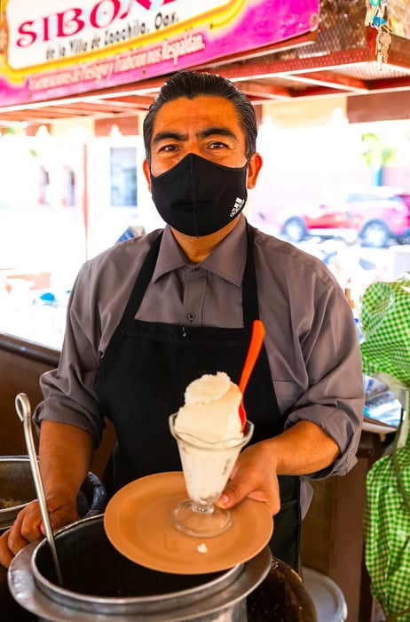 A man in a mask and apron proudly presents a tray filled with a delicious ice cream dish.