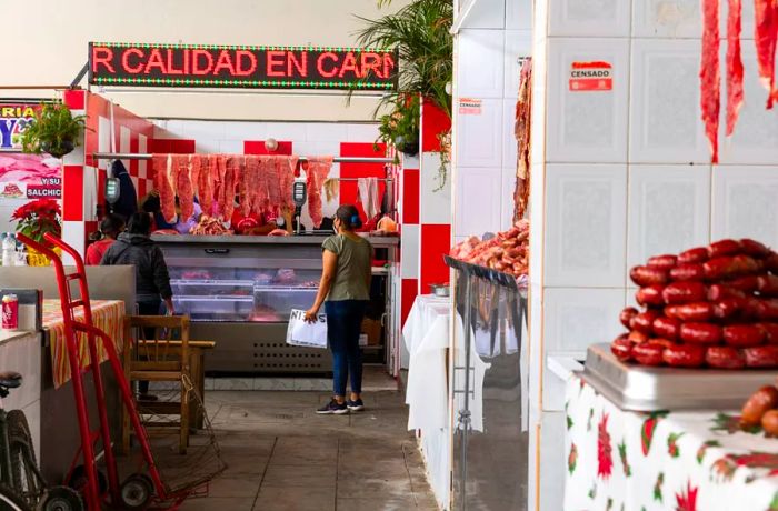 Inside the market, several stalls can be seen. One features a pile of sausages, while another showcases slabs of meat.