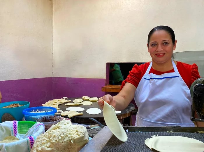 A chef skillfully places tortillas on a comal.