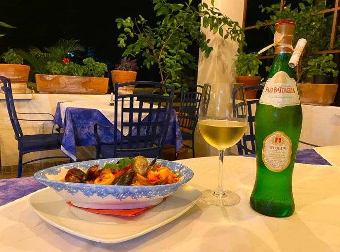 A beautifully presented plate of pasta adorned with mussels and assorted seafood, next to a bottle of wine on a crisp white tablecloth.