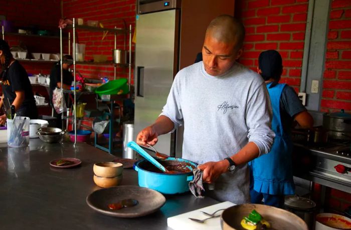 A man ladles mole from a pot on the kitchen counter onto a plate.