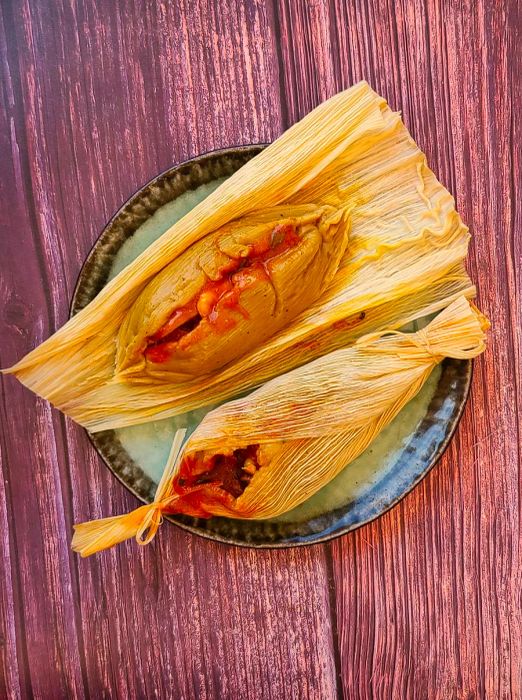 A plate showcasing two tamales de pesco, one partially unwrapped.