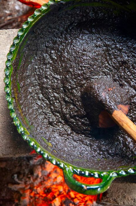 A rich dark mole simmers in a green clay pot over a fire.