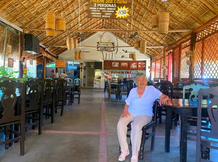 A woman relaxes in a spacious open-air dining room with a thatched roof.