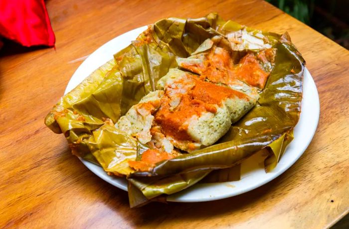 A plate featuring an open tamale topped with rich red mole.