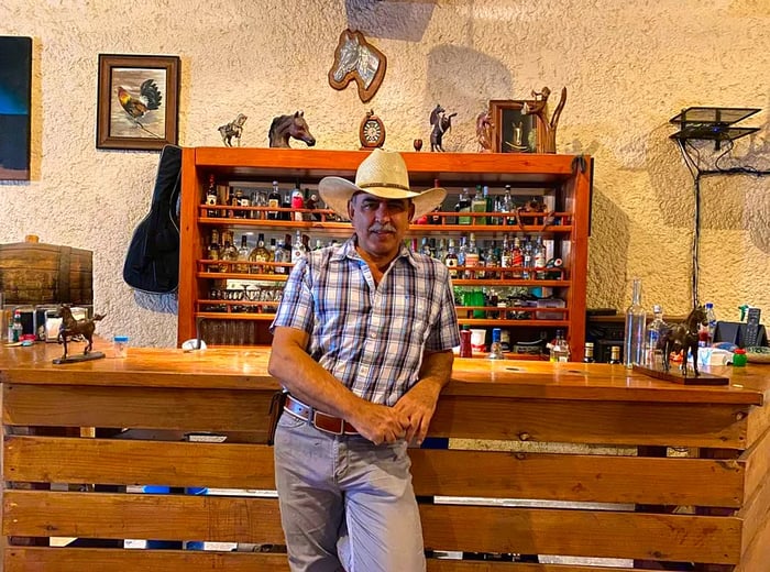 A man in a cowboy hat stands in front of a display adorned with bottles and cowboy-themed decorations.