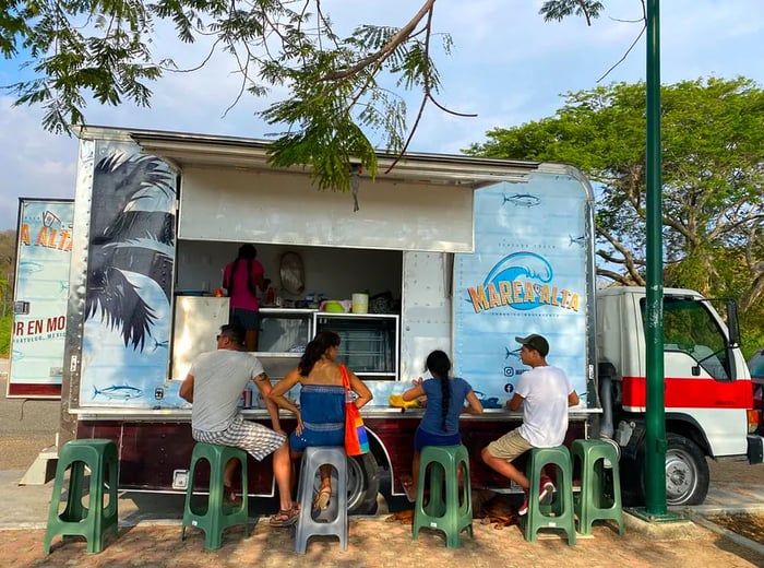 Patrons enjoying their meals on stools next to a food truck.