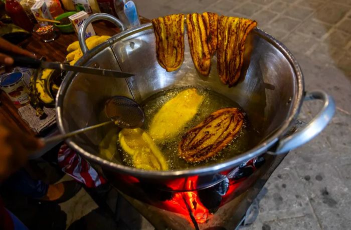 Sliced plantains frying in oil in a large pot.