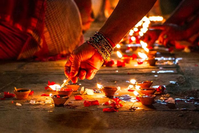 A close-up of a hand lighting incense on the ground in Varanasi at night.