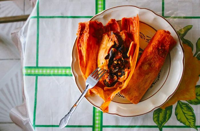 A partially unwrapped tamale filled with mussels still in their shells.