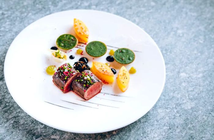 Plates elegantly display slices of rare-cooked meat alongside sides shaped into intricate designs.