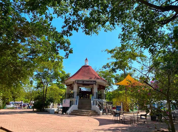 A sunny day showcases a kiosk nestled in a tree-lined park.