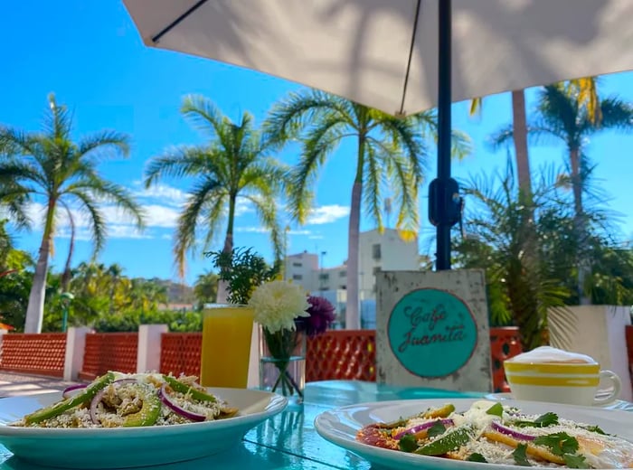 A patio table adorned with fresh salads, offering a view of palm trees on a sunny day.