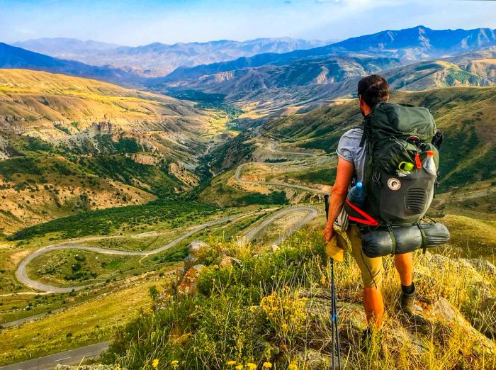 A hiker with a backpack gazes over a valley view in the mountains along the Transcaucasian Trail, Armenia