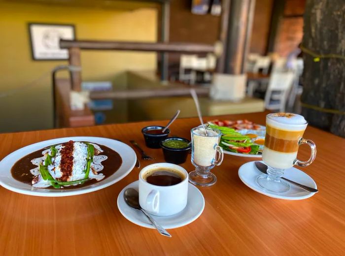 A wooden table showcases an array of dishes accompanied by cups of coffee and elaborate coffee beverages.